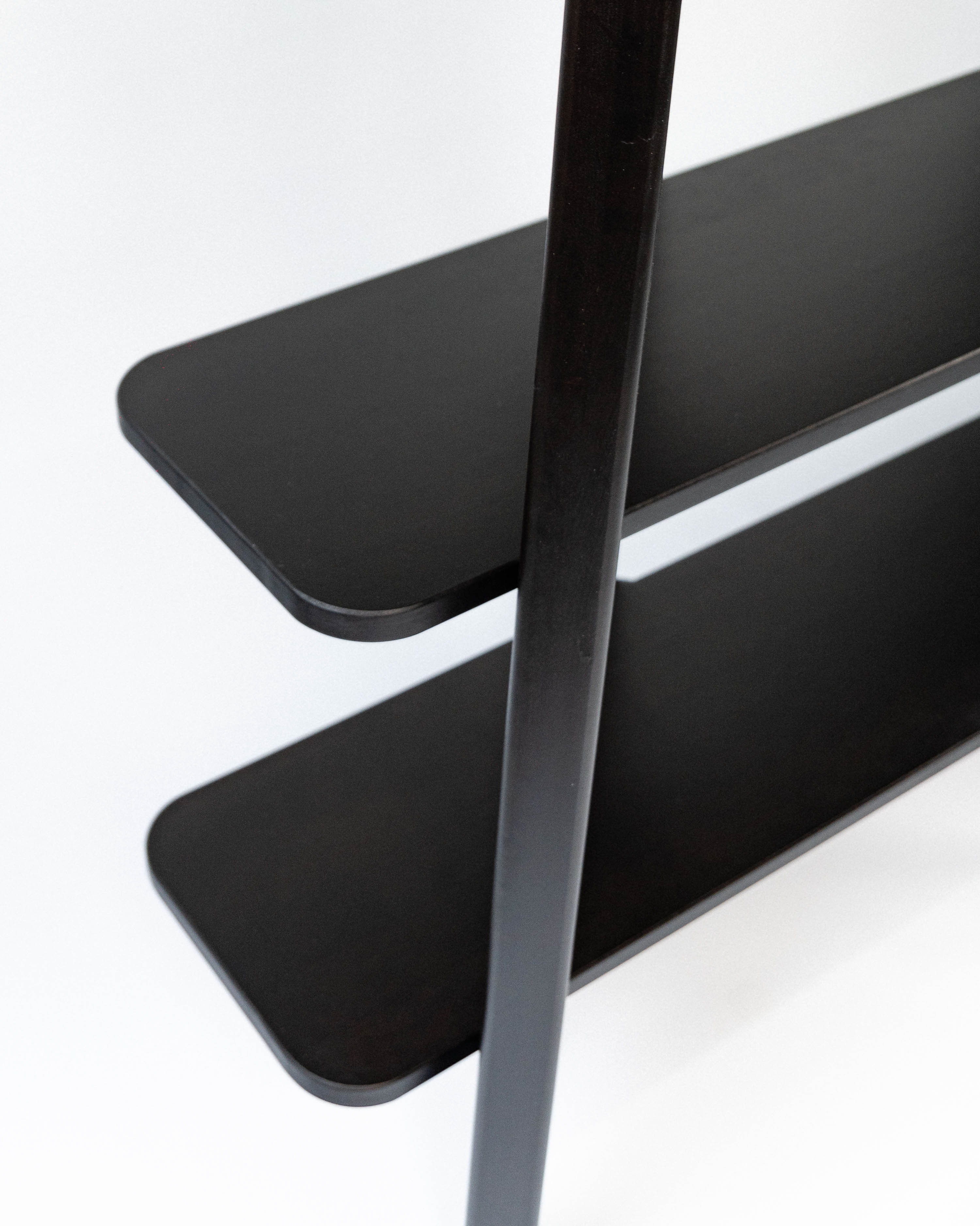 Zbliżenie na detale regału, ukazujące ciemne, zaokrąglone krawędzie drewnianych półek i czarne słupki. Konstrukcja z widocznymi wspornikami.